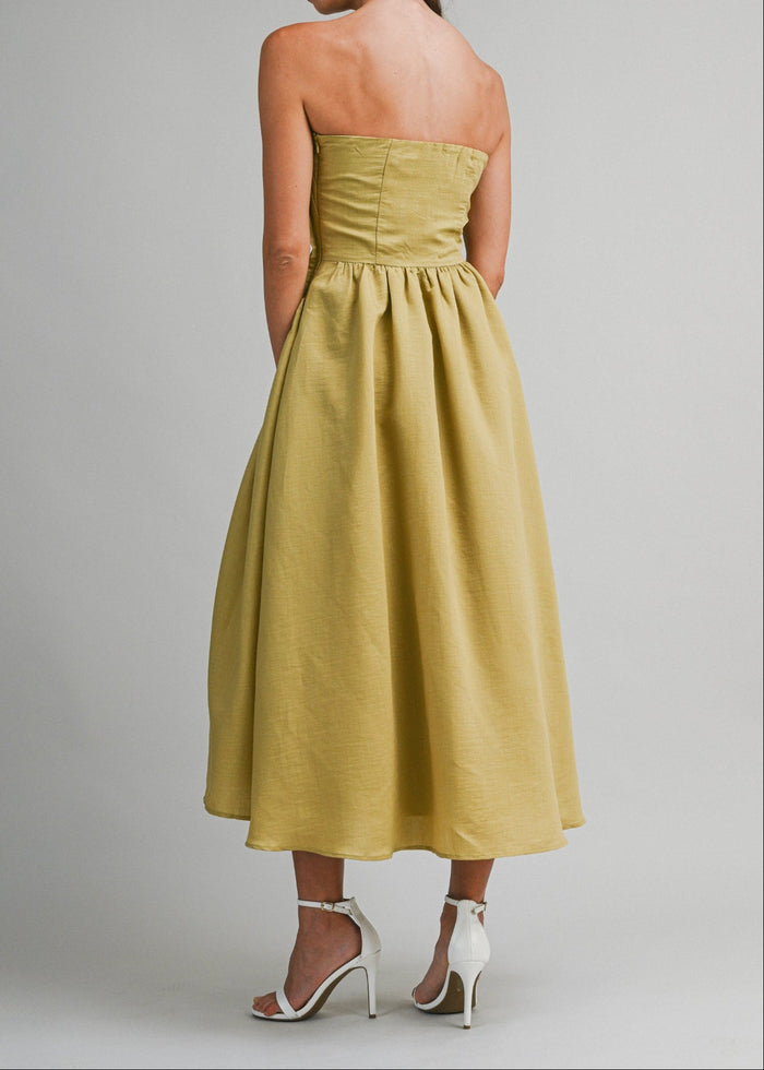 Woman wearing a yellow strapless midi dress with a fitted bodice and full skirt, styled with white heeled sandals.