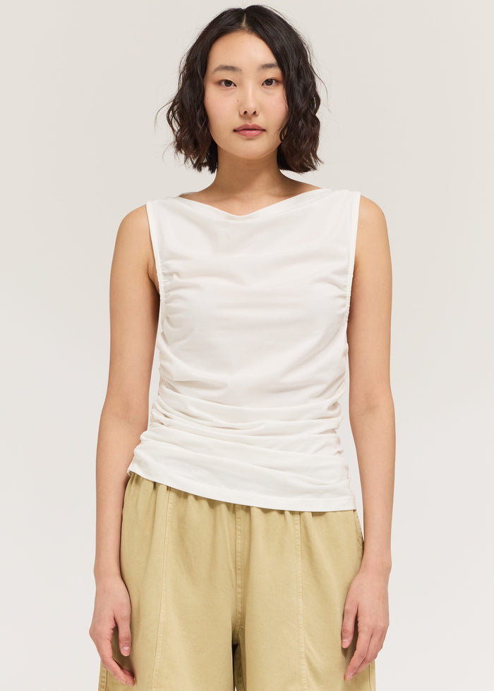 Woman wearing a white sleeveless top and beige shorts on a plain background