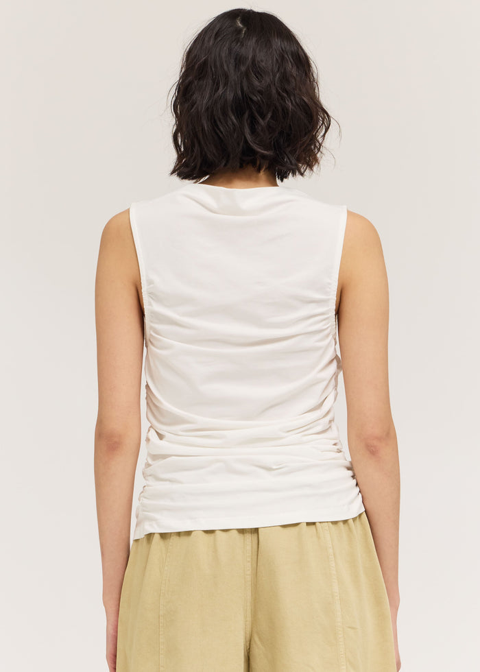 Person wearing a white sleeveless top and beige pants on a plain background