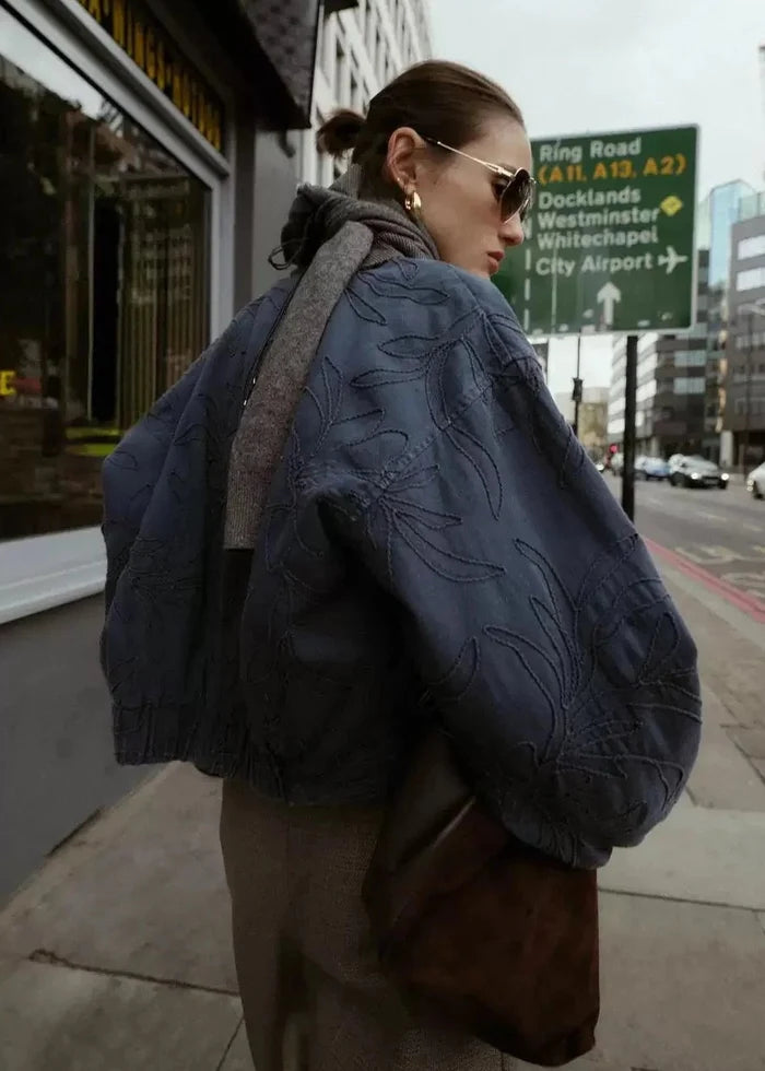 Navy quilted zip-up jacket with leaf pattern, worn over gray sweater.