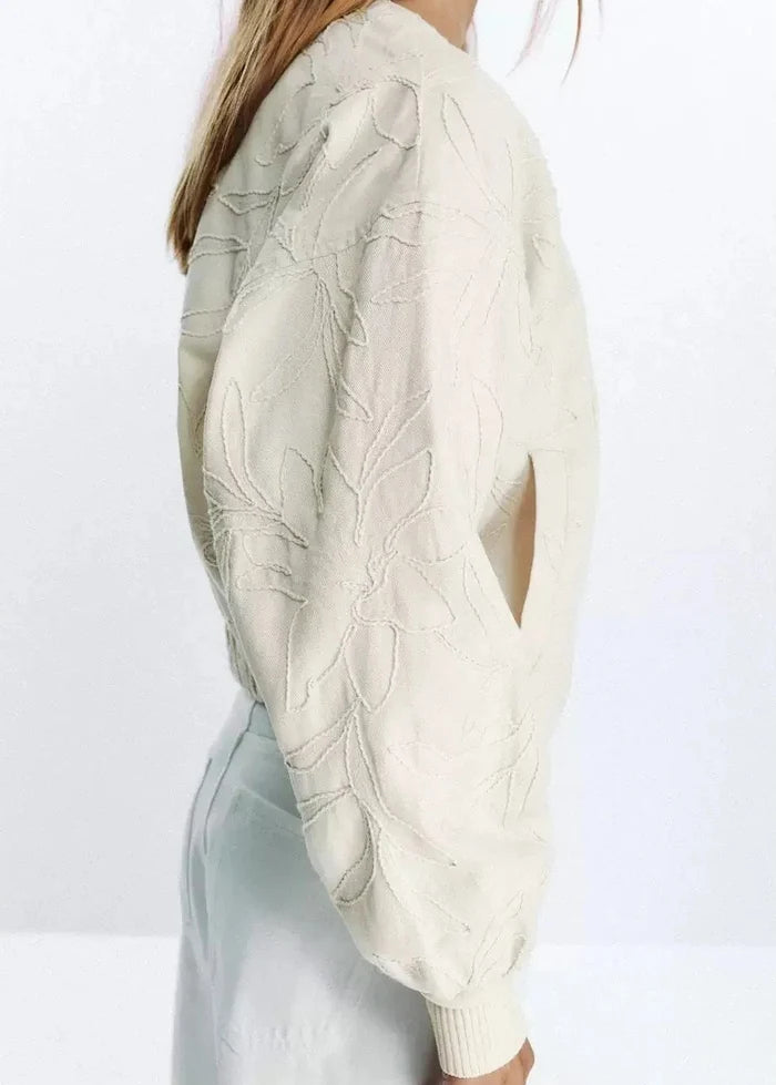 Cream zip-up jacket with quilted leaf pattern, shown from side view on model wearing light blue pants.