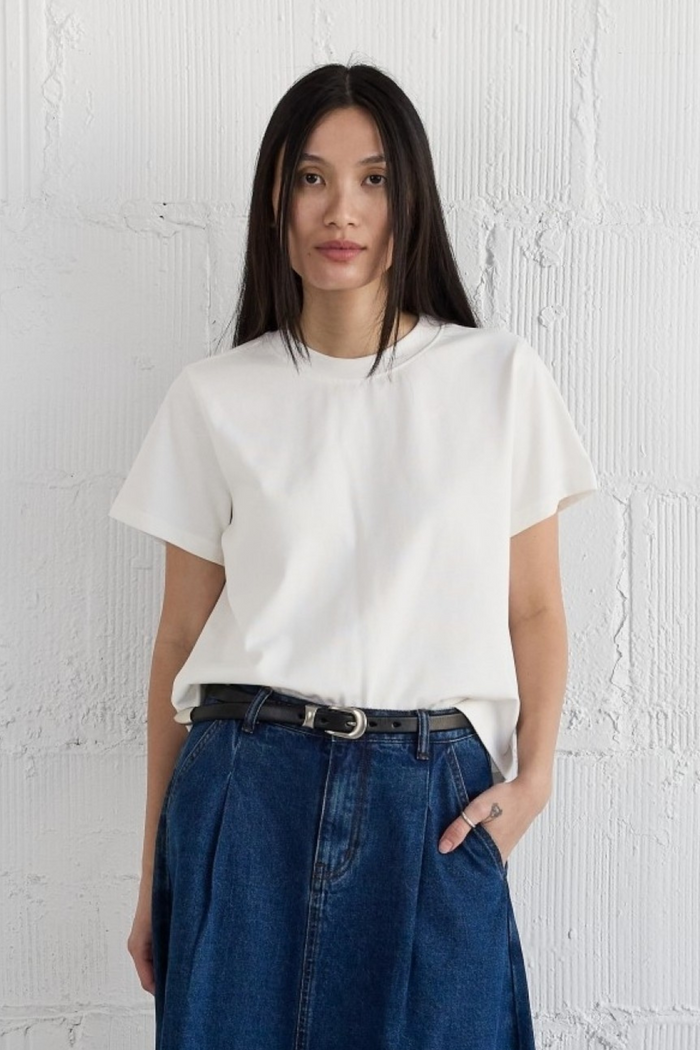 Woman wearing cream short-sleeve crew neck top with blue denim jeans and black belt.