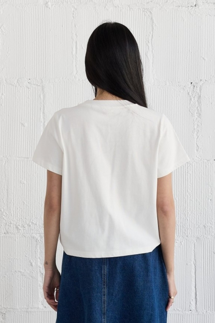 White short-sleeve top with crew neckline on model wearing dark denim skirt, back view.