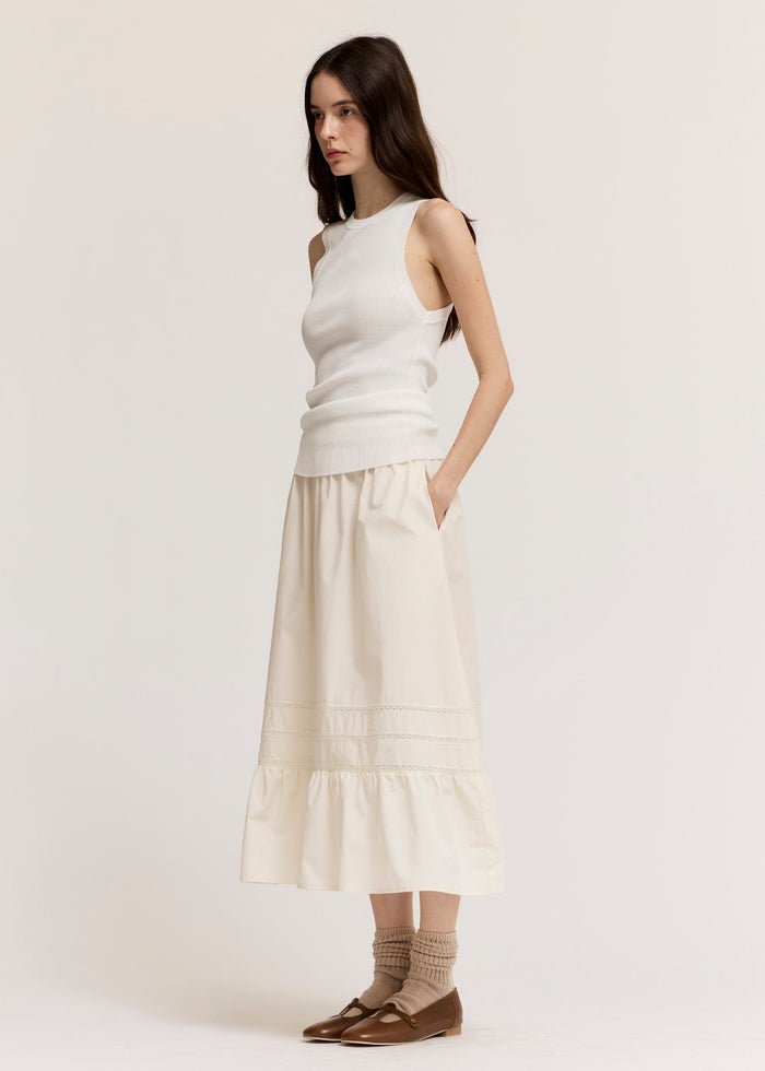 Woman wearing cream ribbed sleeveless knit tank top with cream tiered midi skirt and brown flats.