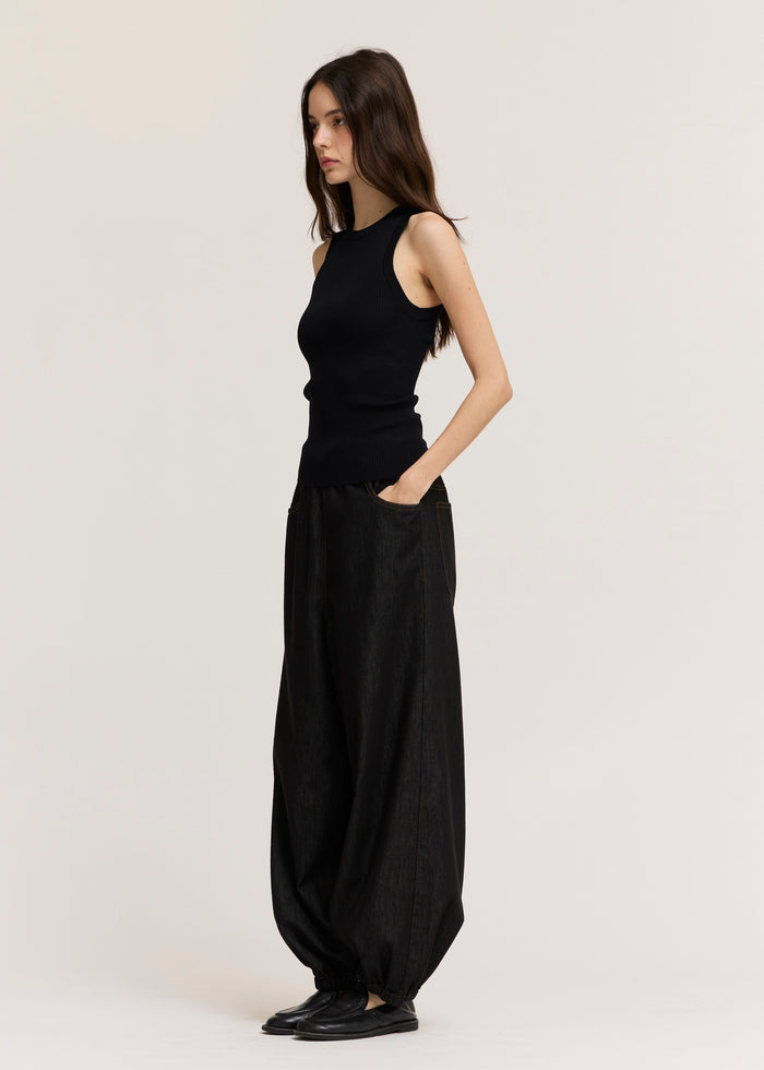 Black ribbed sleeveless tank top worn with black denim pants and black shoes.