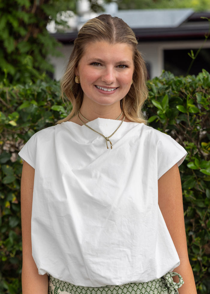 White short-sleeve top with gathered bubble hem, worn with patterned green skirt.