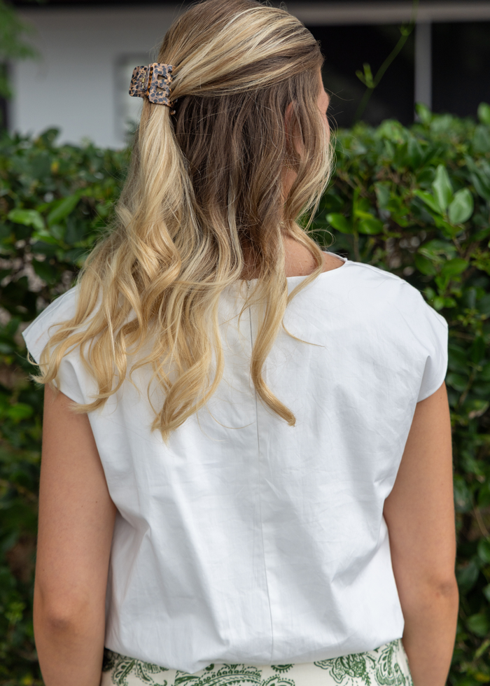 Woman wearing white short-sleeve top with bubble hem, shown from back view outdoors.
