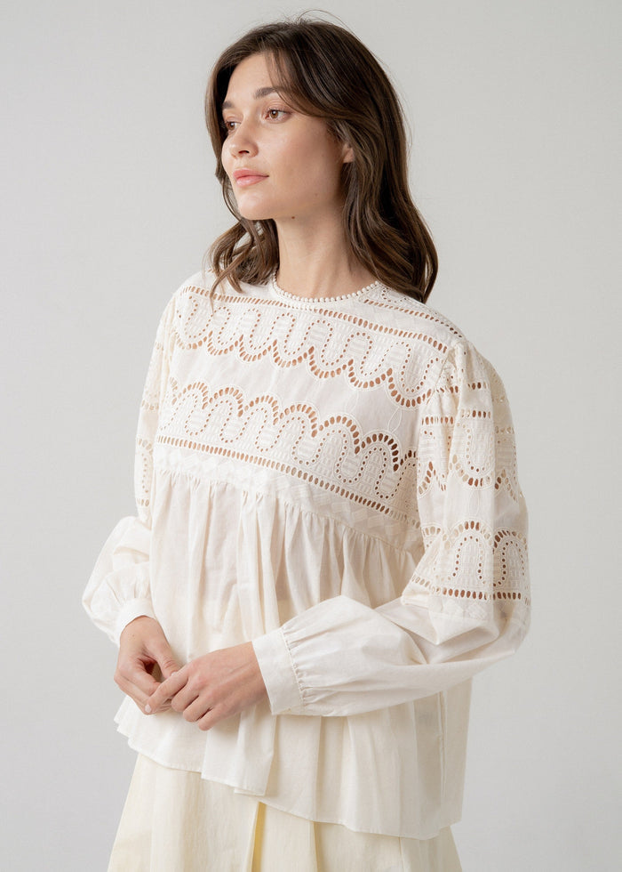 Cream eyelet longsleeve blouse with gathered waist and babydoll silhouette on model.