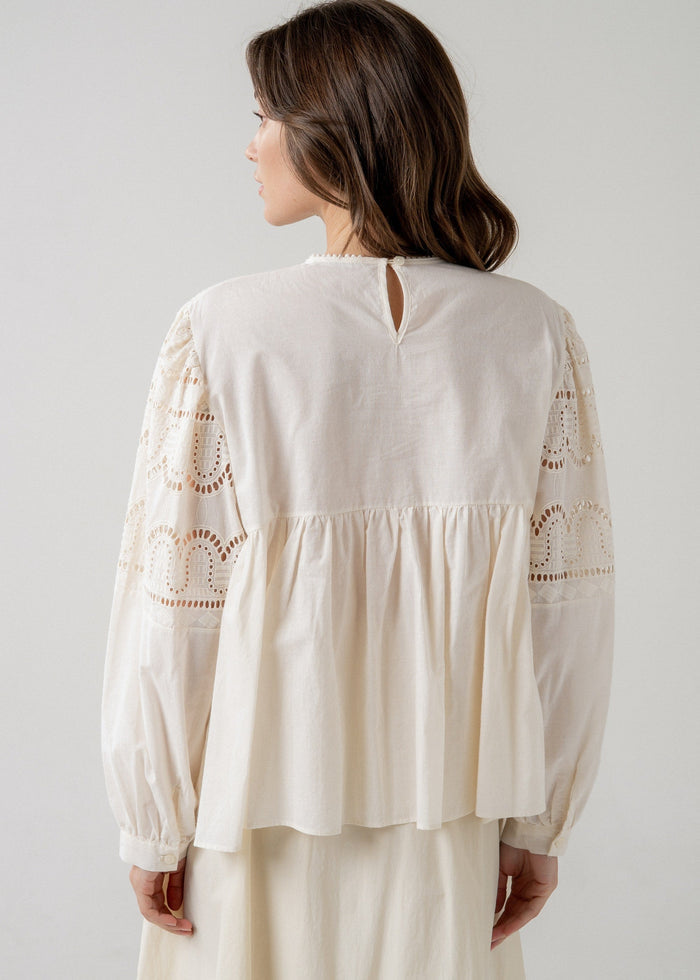 Cream longsleeve babydoll blouse with lace eyelet sleeves and gathered waist, worn with back keyhole opening visible.