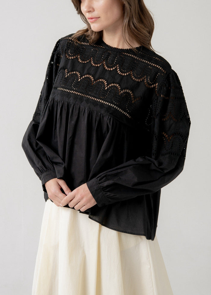 Black long-sleeve blouse with lace yoke and scalloped cutout details, relaxed babydoll silhouette with gathered waist.