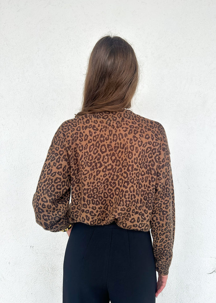 Tan and brown leopard print crewneck sweater with long sleeves, shown from back on model wearing black pants.