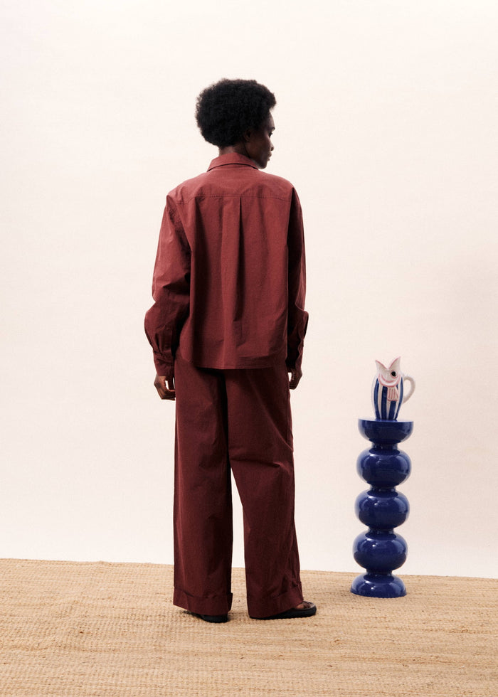 Burgundy button-down shirt with long sleeves worn by person standing, shown from back view.