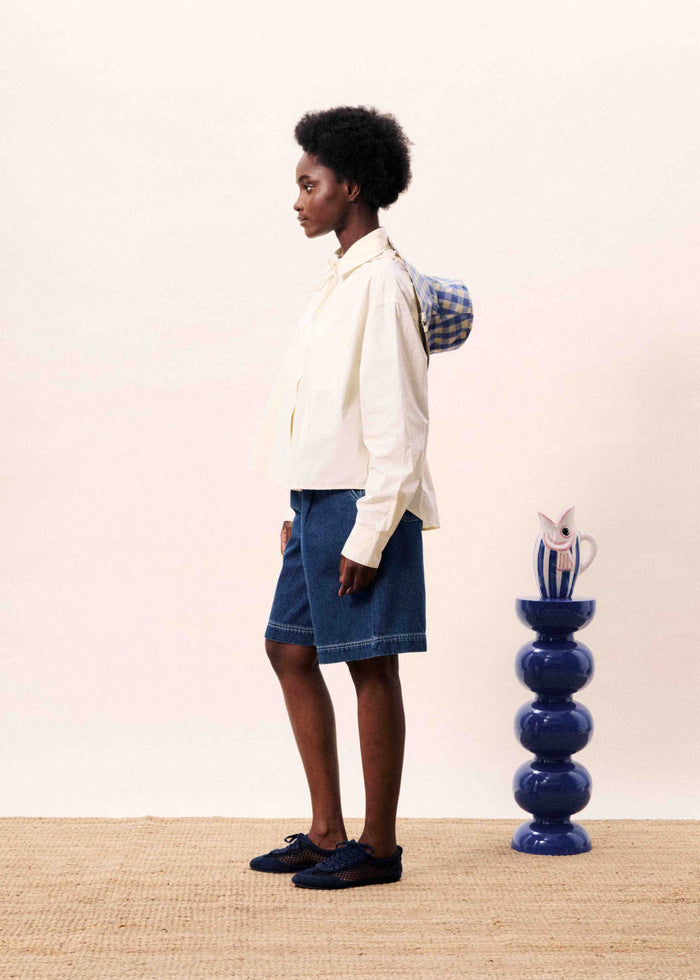 Cream button-down shirt with long sleeves worn with a denim skirt and navy loafers, styled from the side.