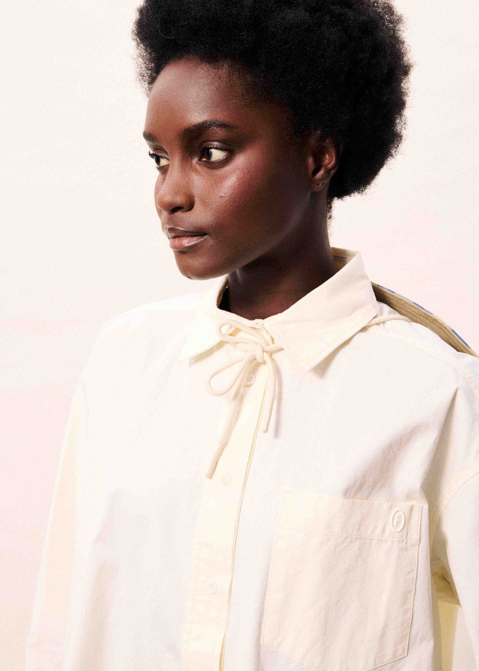 Cream button-down shirt with drawstring neckline and contrast shoulder stripe on model.