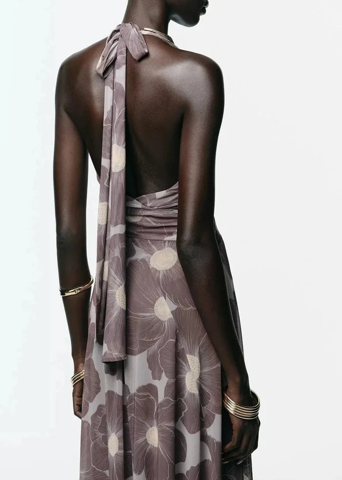 Woman wearing mauve halter maxi dress with cream floral print and open back with tied straps.
