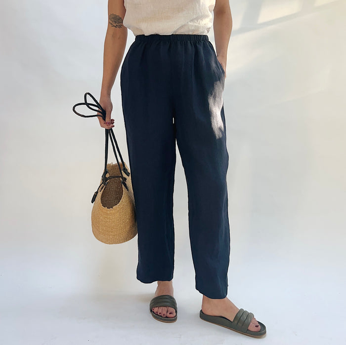 Person wearing navy linen pants holding a woven bag on a white background
