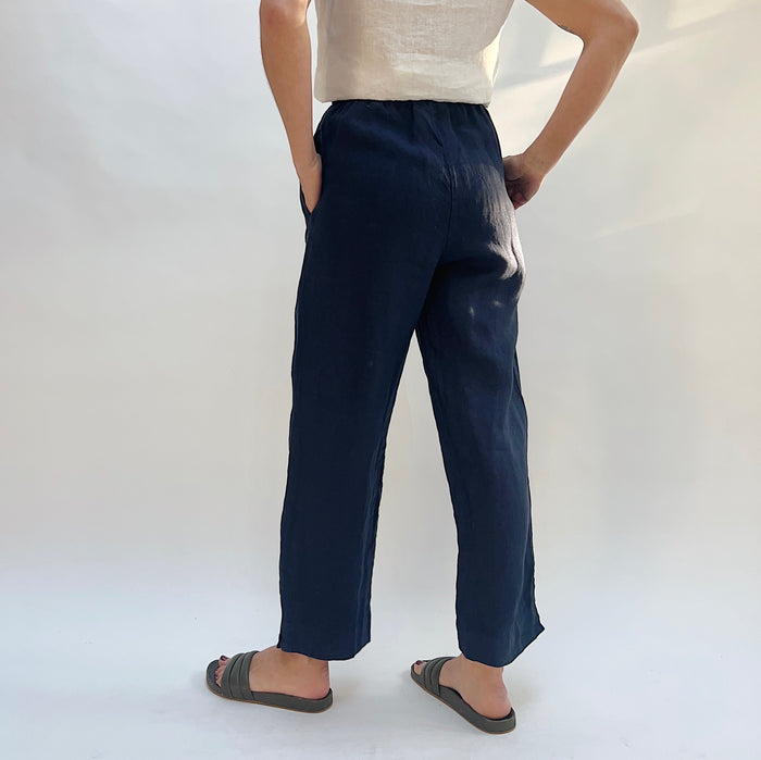 Person seen from behind wearing navy pants and a white top on a plain background