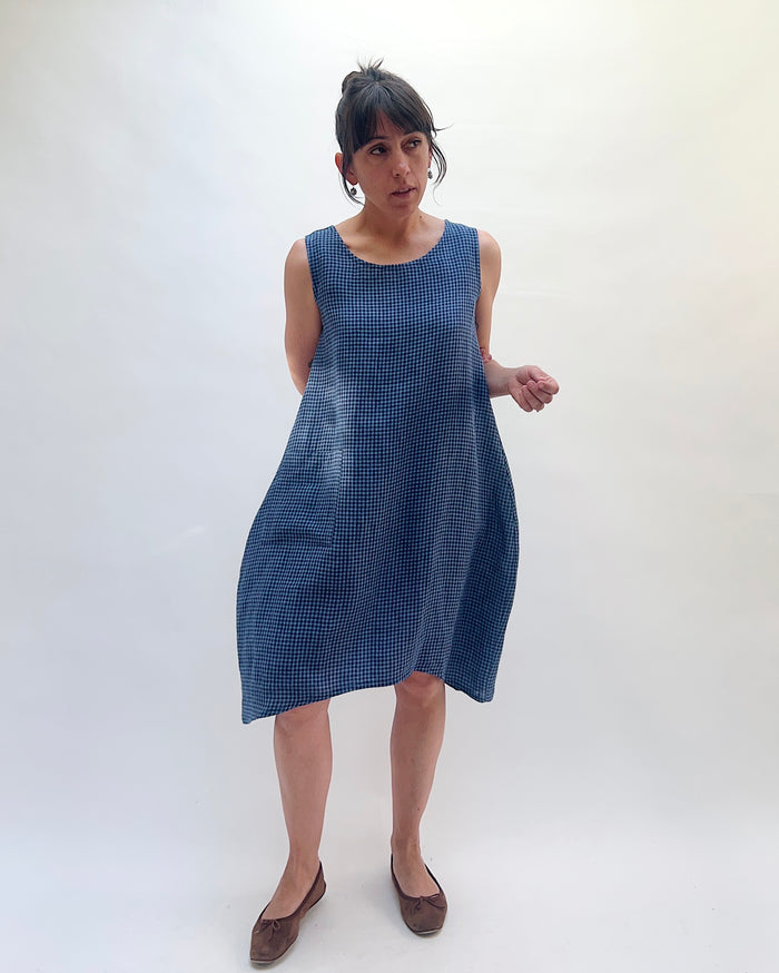 Front view of Christopher Calvin Linen Mini Check Dress in navy-and-white mini check, showing the scoop neckline, relaxed A-line silhouette, side pockets, and asymmetric hem, worn with brown ballet flats on a white background