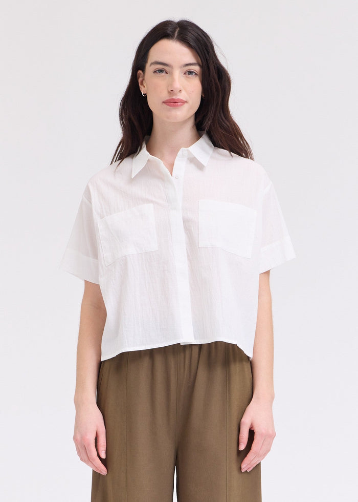 White short-sleeve button-up top with collar and chest pocket, cropped fit.