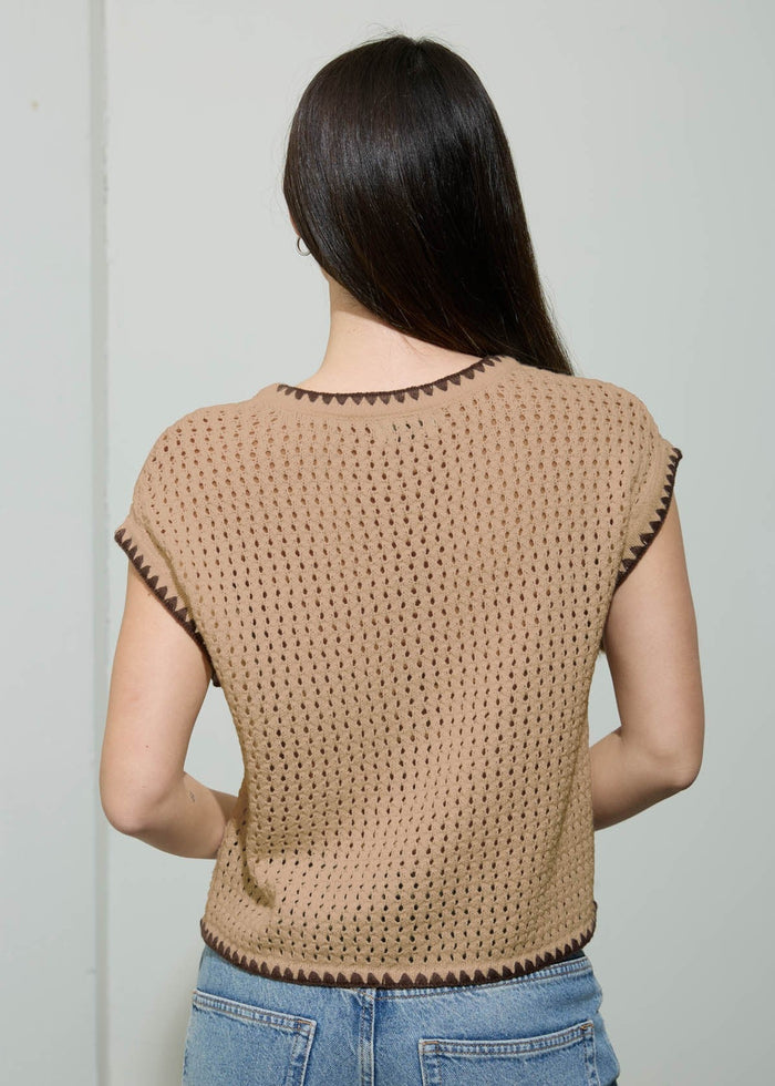 Woman wearing a beige crochet top and blue jeans against a plain background