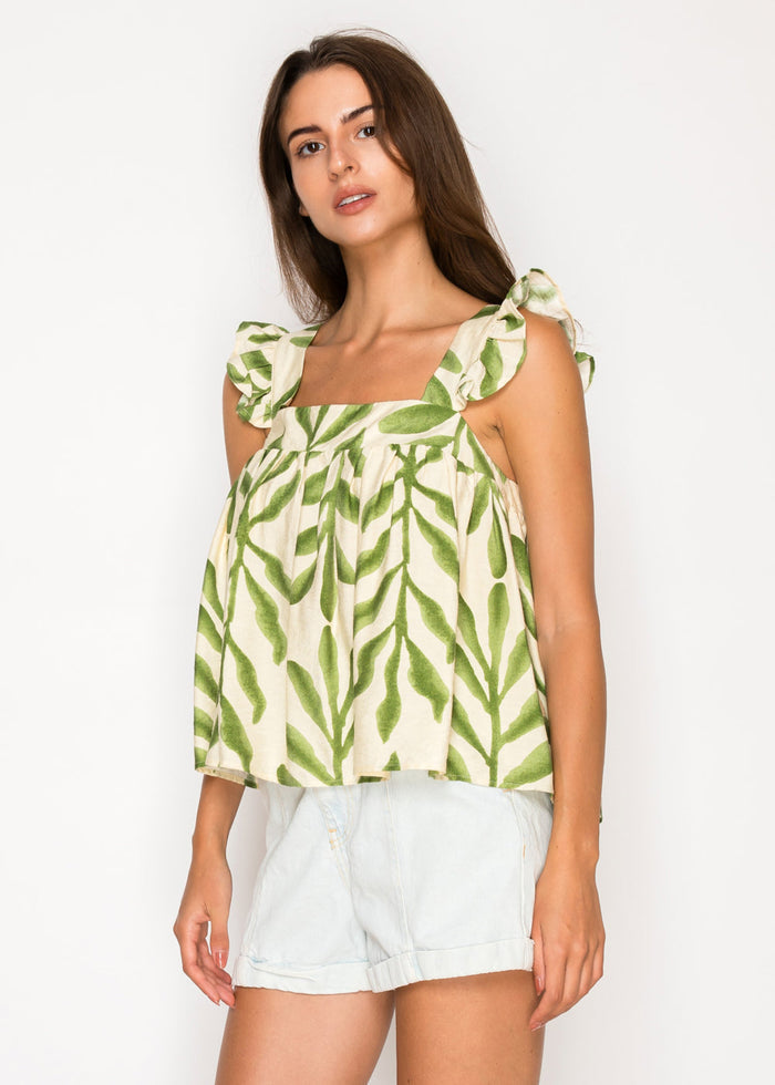 Woman wearing cream-colored sleeveless top with green leaf print and tie-shoulder straps, paired with white denim shorts.