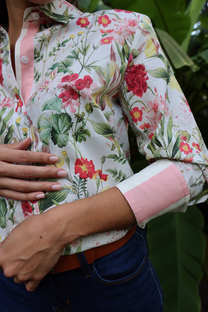 White button-down shirt with red, pink, and yellow floral print and pink rolled cuffs.