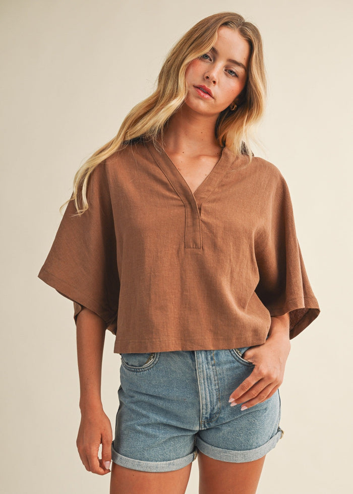 Brown linen popover top with collar and short sleeves worn with denim shorts.