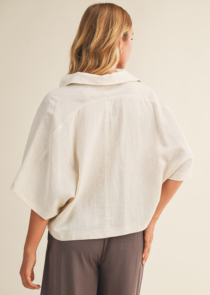 Cream linen popover top with collar and three-quarter sleeves, shown from back on model wearing gray pants.
