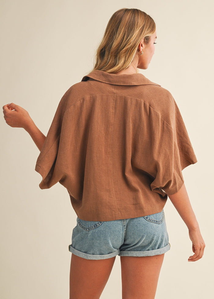 Woman wearing a tan popover collar top with short puffed sleeves, paired with rolled denim shorts.