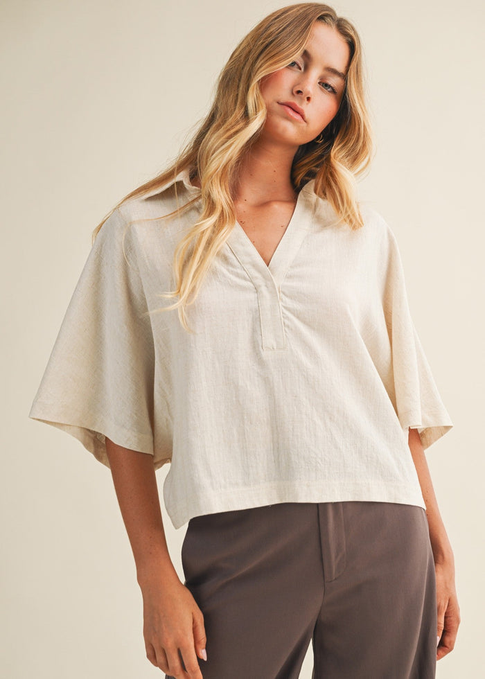Cream linen popover top with collar and flutter sleeves paired with charcoal pants.