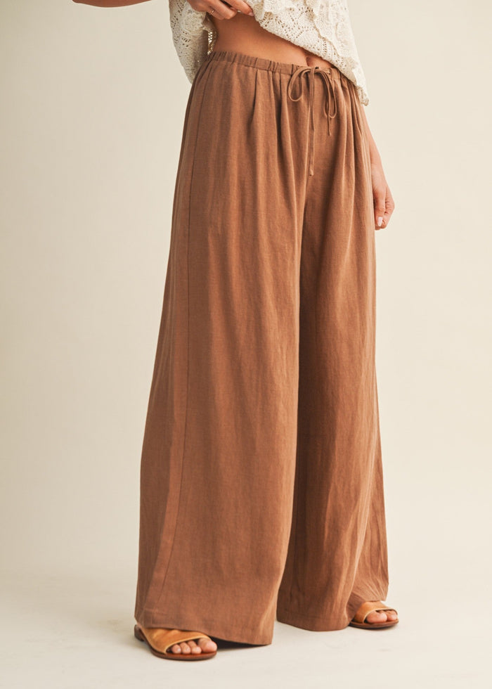 Tan wide-leg pants with drawstring waist and relaxed fit, styled with cream knit top and tan sandals.