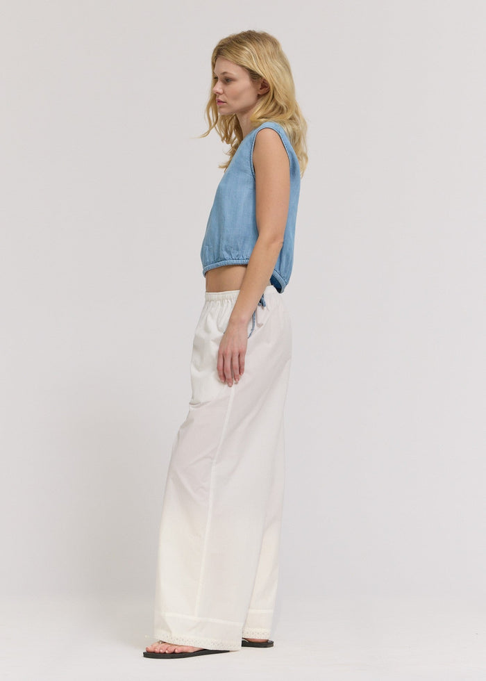 Woman wearing a light blue sleeveless chambray shell top with a cropped fit and white wide-leg pants.