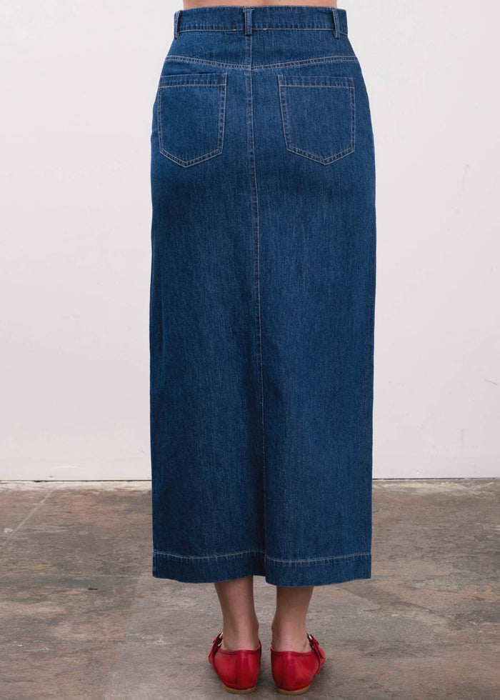 Blue denim midi skirt with back patch pockets and center seam, shown from behind.