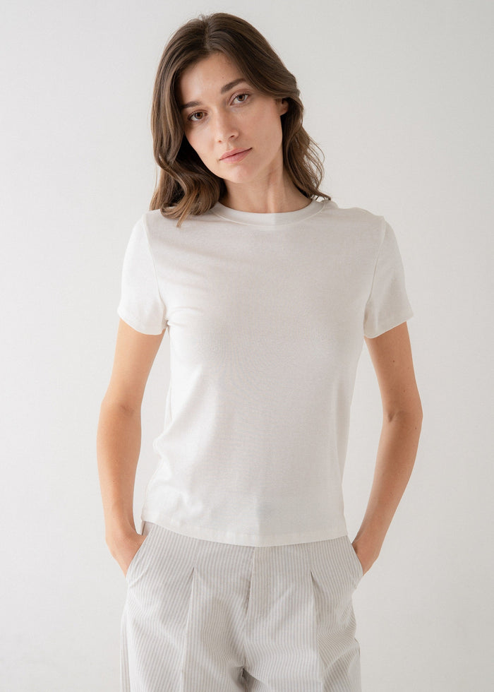 Woman wearing a white crew neck short-sleeve t-shirt with neutral-toned striped pants.