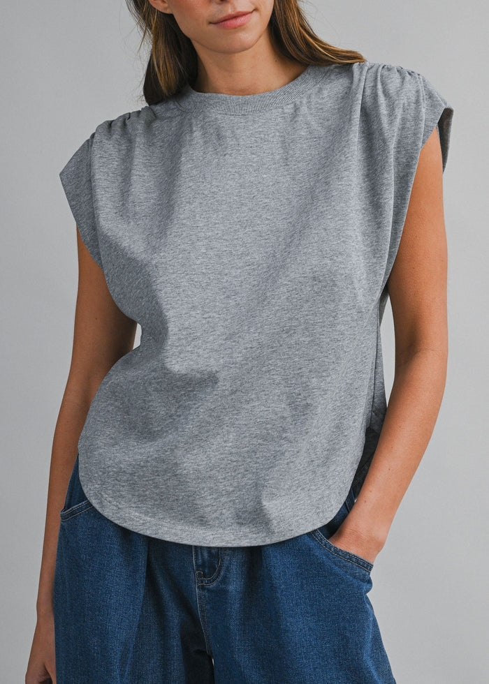 Woman wearing a gray sleeveless top and blue pants against a gray background