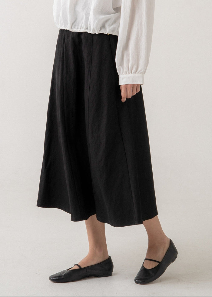 Black a-line midi skirt with high waistband worn with white long-sleeve top.