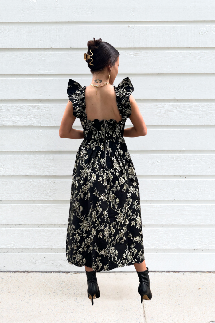 Black midi dress with cream floral print, ruched bodice, flutter sleeves, and open back design.