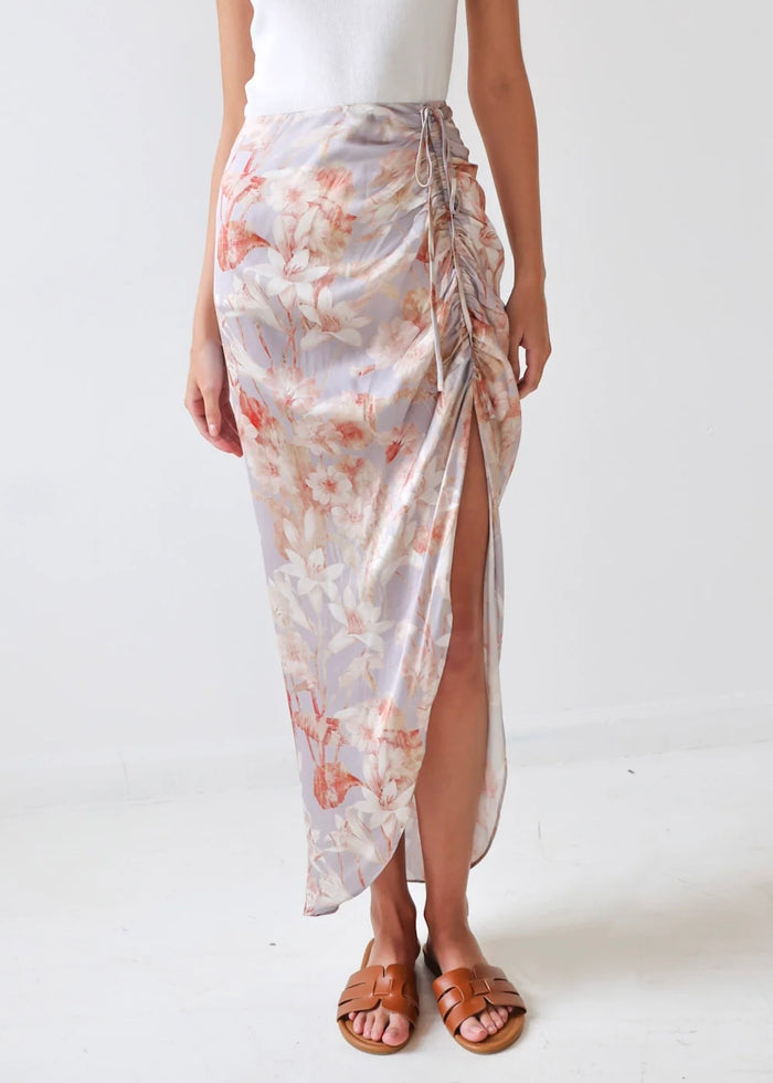 Wrap skirt with pink and coral floral print, side tie closure, and high slit, worn with white tank top and tan sandals.