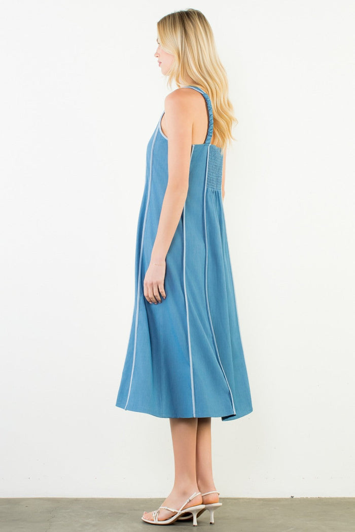 Blue denim sleeveless dress with thin straps and A-line silhouette, shown on model from side angle.