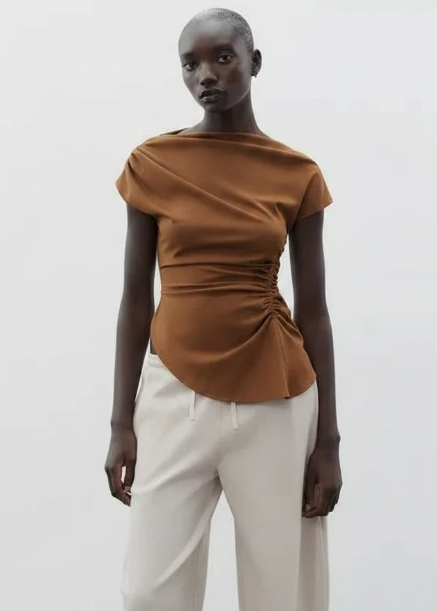 Camel boatneck top with ruched side detail and short sleeves, paired with white trousers.