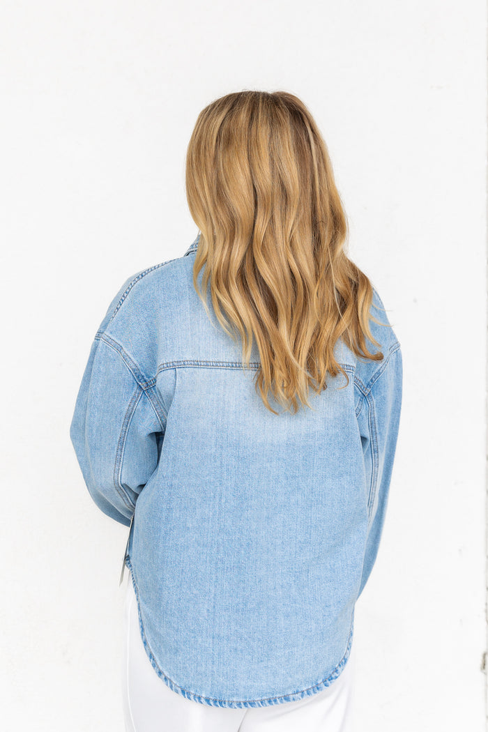 Light blue denim shirt with button front and chest pocket, worn by model shown from back view.