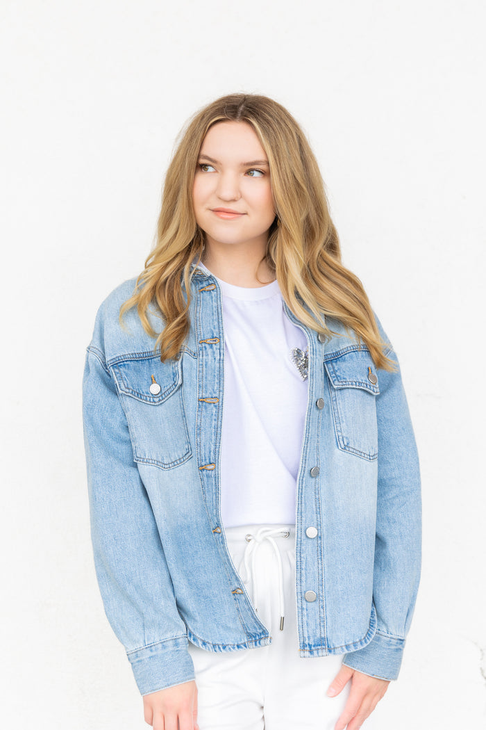 White graphic t-shirt with small dark design worn under a light wash denim jacket.