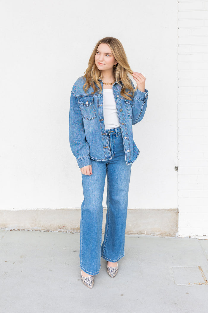 Woman wearing a light blue denim jacket over a white top with matching blue jeans and metallic pointed-toe heels.