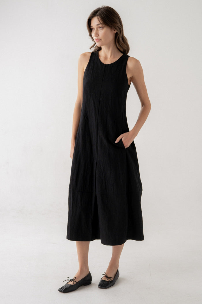 Black sleeveless midi dress with round neckline, center button detail, and side pockets on model.