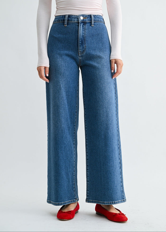 Woman wearing blue high-rise wide-leg jeans with white long-sleeve top and red slip-on shoes.