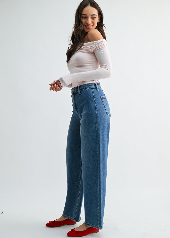 Woman wearing high-rise medium-wash jeans with a white off-shoulder top and red slippers.
