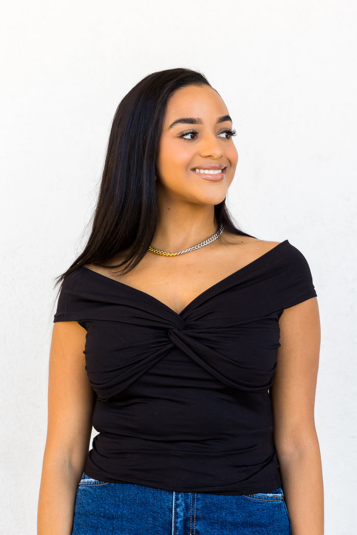 Black off-the-shoulder top with twisted front detail and short sleeves.