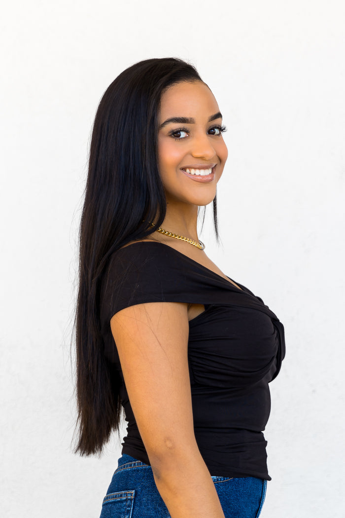 Black off-the-shoulder top with ruched fabric worn with blue jeans.