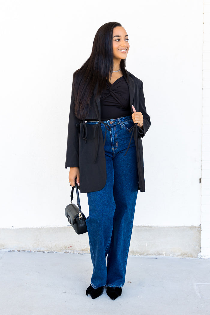 Black off-the-shoulder wrap top with ruched neckline worn with blue jeans and black blazer.
