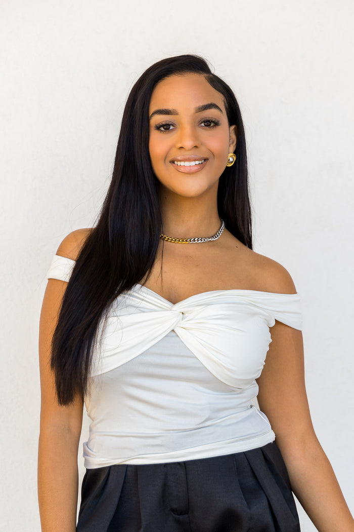 White off-the-shoulder top with twisted front detail and ruched sides, paired with black skirt.